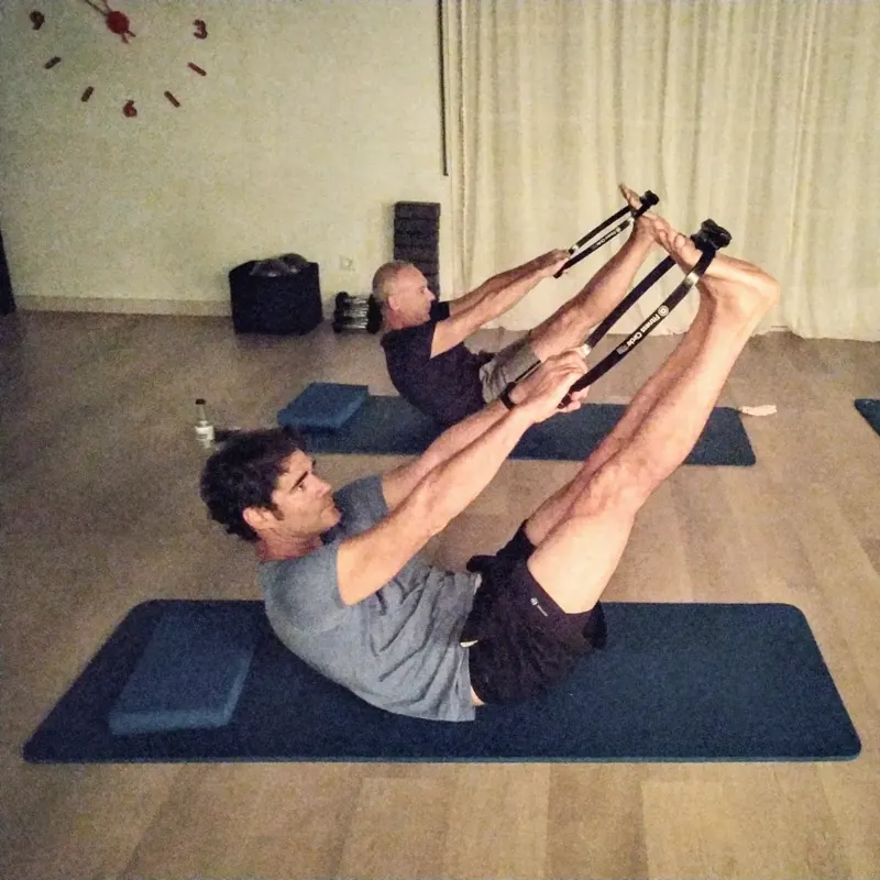 Dos alumnes fent Pilates Mat amb aro, asseguts en equilibri amb les cames enlaire